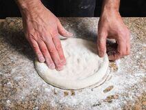in this image men is pressing the pizza dough on a flat surface